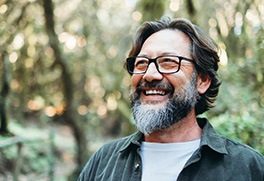 a smiling man with glasses standing in a forest
