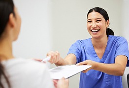 a friendly dental staff member handing a patient forms