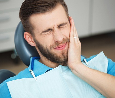 Man holding cheek in pain after emergency dentistry