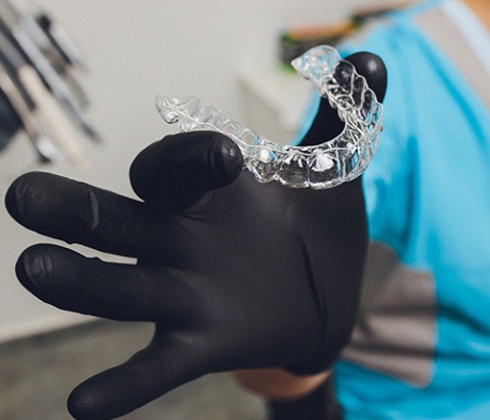 An up-close image of a dental professional wearing a black glove and holding an Invisalign aligner in Cleburne
