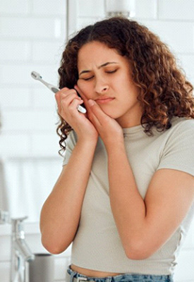 Woman holding her aching jaw and a toothbrush