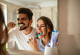 A man and woman brushing their teeth in front of a bathroom mirror