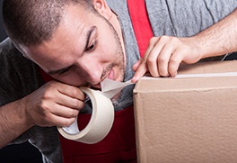 A man tearing tape packaging with his teeth