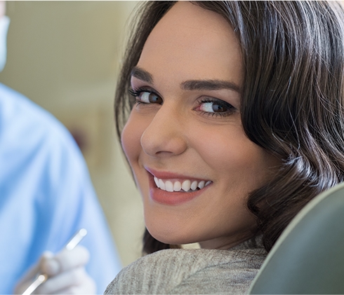 Woman smiling over shoulder after receiving dental services