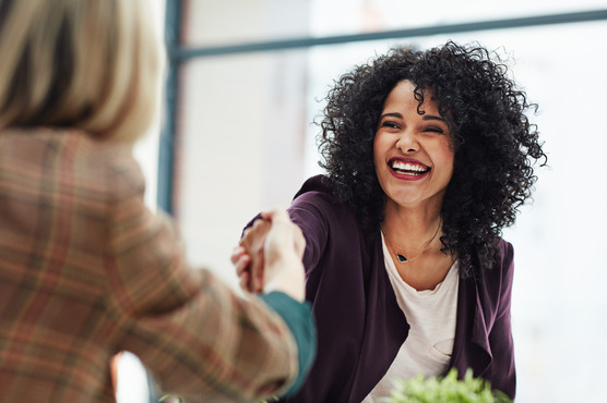 woman smiling while shaking someone’s hand 