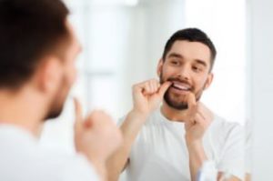 Smiling man flossing in the mirror