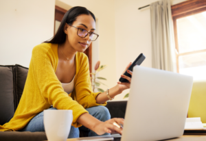a woman holding a phone and looking at a laptop